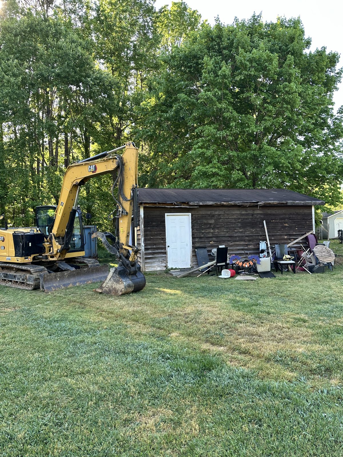 Excavator staged next to a shed and debris pile before demolition